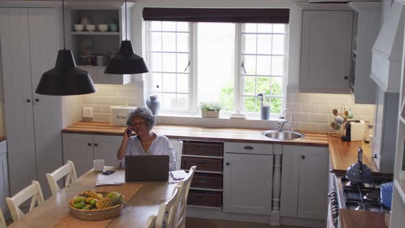 Senior african american woman using laptop and talking on smartphone at home