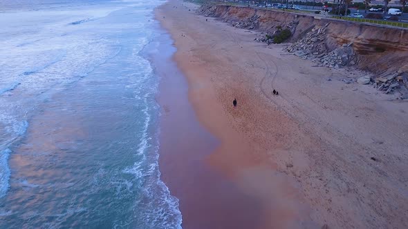 Drone shot of a person walking on an empty beach, with their dogs, just before sunset. Video was sho