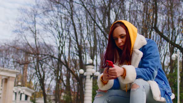 Young Woman with Mobile Phone in City Park