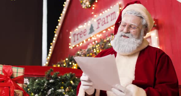 Portrait of a Cute Joyful Santa Claus Reading Letters in a Beautiful New Year's Decorated Studio