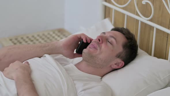 Cheerful Young Man Talking on Smartphone in Bed