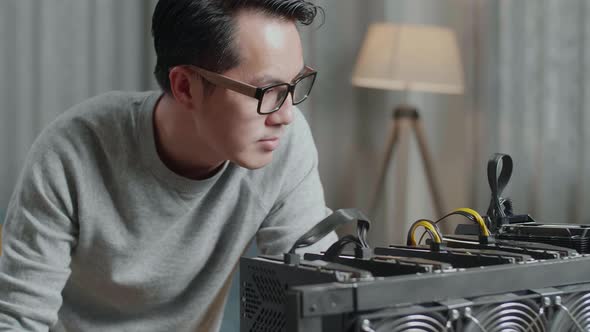 Close Up Of Satisfied Asian Man Looking At The Mining Rig For Mining Cryptocurrency While Working