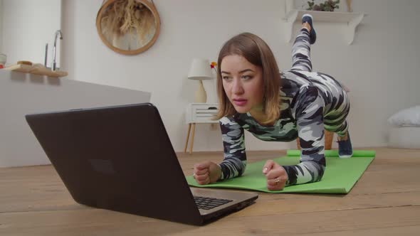 Charming Sporty Fit Woman Doing One Legged Plank Yoga Exercise During Online Class at Home