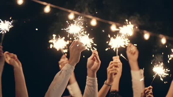 Closeup of Hands or Palms Holding and Waving Burning Sparklers in Front of Black or Dark Background