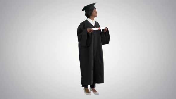 Smiling African American Female Student in Graduation Robe Posing with Diploma on Gradient