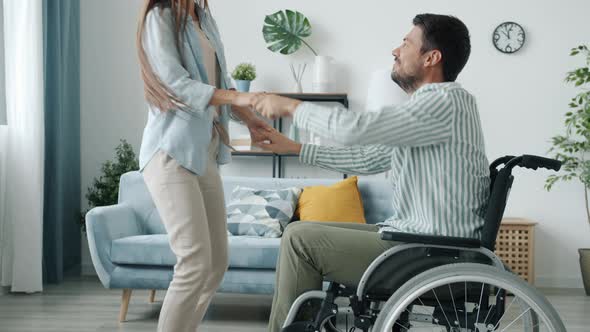 Handicapped Young Man in Wheelchair Dancing with Happy Young Lady at Home