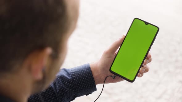 A Man Listens to Music on a Smartphone (Vertical) with Green Screen  Closeup From Behind