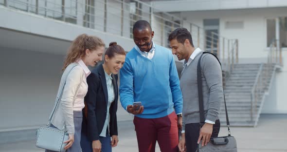 Diverse Colleagues Watching Content on Smartphone and Laughing Outdoors