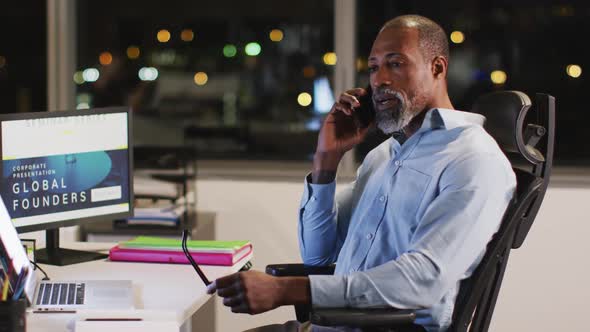 Professional businessman talking on his phone while sitting on his desk in modern office in slow mot