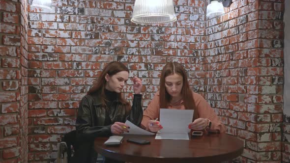 Two Girls are Working in a Cafe with Documents