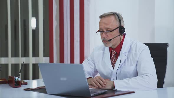 Online Medical Consultancy. Senior old doctor wears headset looking at camera