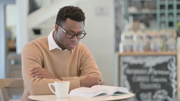 African American Man Reading Book While Drinking Coffee in Cafe