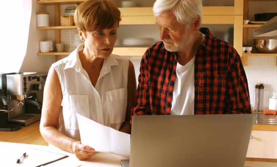Senior couple paying bills online on laptop in kitchen