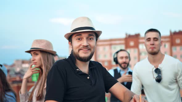 Pretty Brutal Caucasian Man in Hat Surrounded By Friends Dancing and Having Fun at Rooftop Party