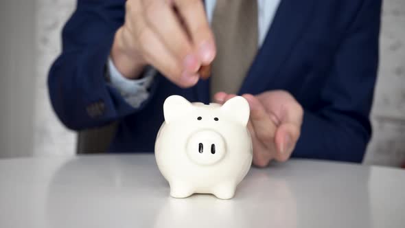 Business Man Putting Coins in White Piggy Bank Indoors  Business Money Saving and Finance Concept