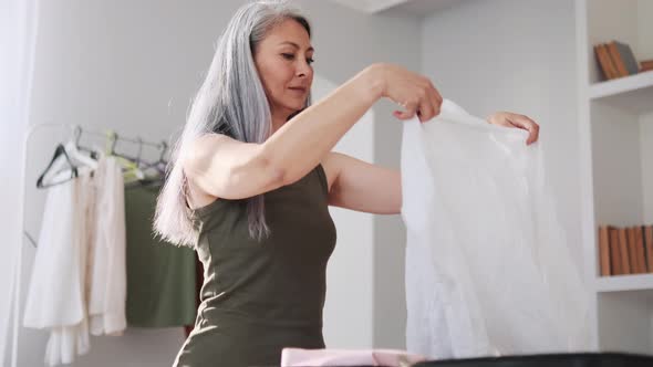 Asian concentrated woman packing things in a suitcase