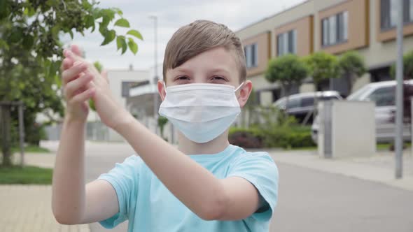 A Young Boy Puts on a Face Mask and Applauds To the Camera in an Empty Suburban Area - Closeup