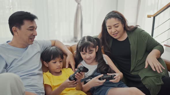 Happy family adult parents with cute kids relax on sofa playing video game having fun with together.