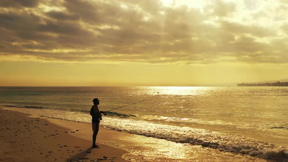 Sun rays showing through the dramatic clouds above the sandy beach with lonely fisherman fishing in