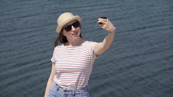 A Young Woman is Filming Herself Against the Backdrop of Water on a Warm Summer Day