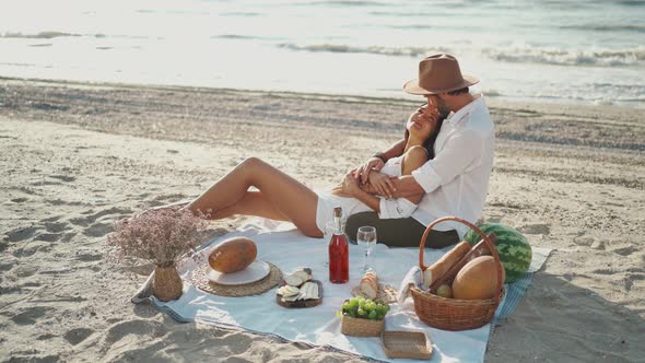 Elegant Romantic Couple Having Picnic at the Beach Embracing and Lying Blanket