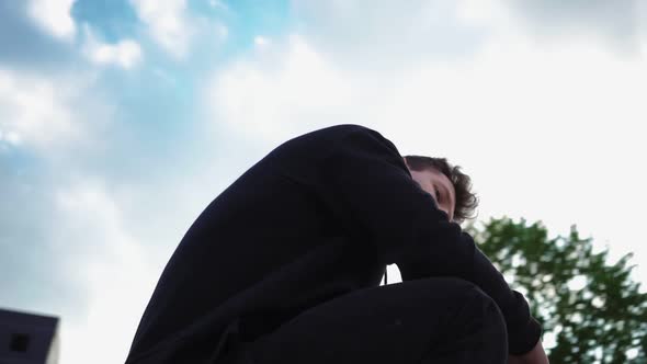 Stylish Man in a Black Hoodie Sits in City Park and Looks at Camera