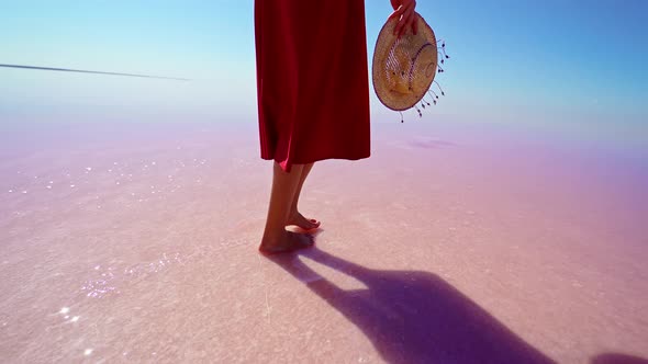 Woman Legs in Red Skirt Walking on Salt White Beach Holding Straw Hat