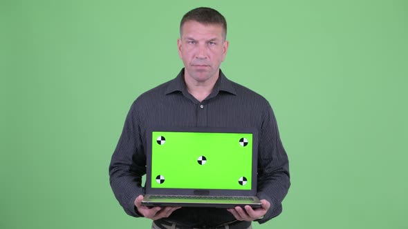 Angry Macho Mature Businessman Showing Laptop