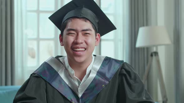 Asian Man Wearing A Graduation Gown And Cap Having Video Call In Living Room