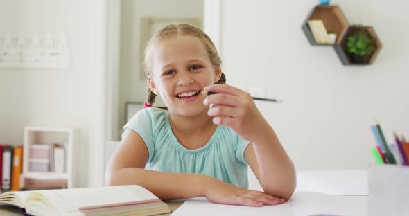 Portrait of caucasian girl holding a pencil smiling looking at the camera at home