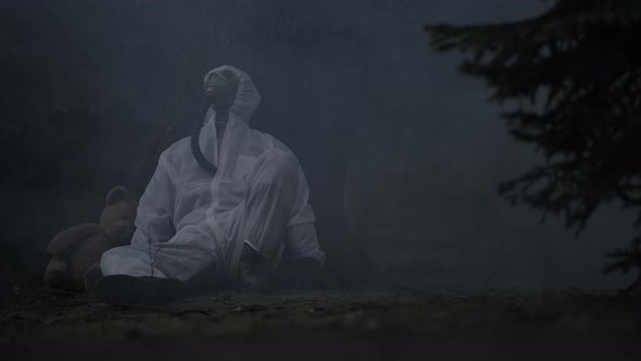 Hopeless Men Wearing Chemical Gas Mask Seating Next to Teddy Bear Inside Polluted Forest