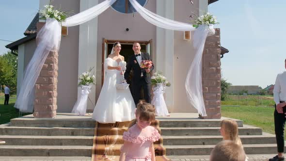 A Beautiful Young Couple Comes Out of the Church and Scatters Candy to the Children