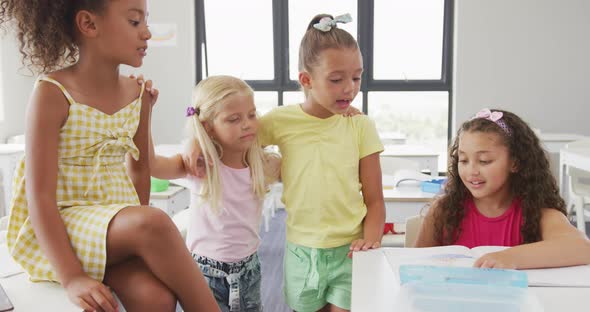 Video of happy diverse girls sitting at school desk, talking and laughing