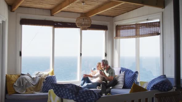 Happy caucasian mature couple drinking coffee and talking in sunny living room