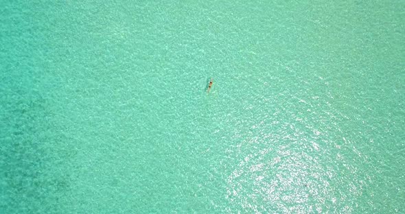 Aerial drone view of a woman floating and swimming on a tropical island.