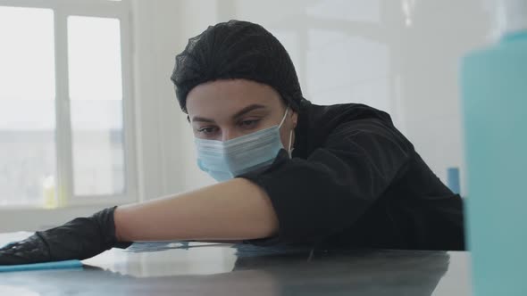 Closeup Portrait of Concentrated Woman in Coronavirus Face Mask Disinfecting Table in Commercial