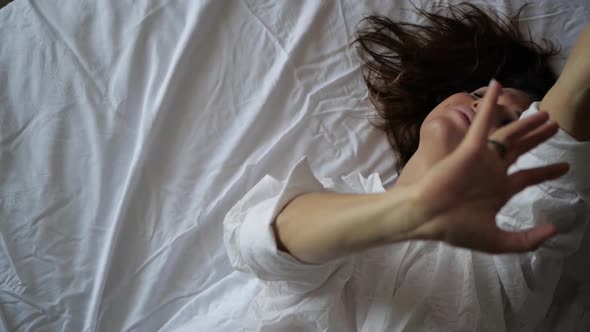 Sexy Woman Brunette Dancing with Her Hands Lying on White Bed Linen