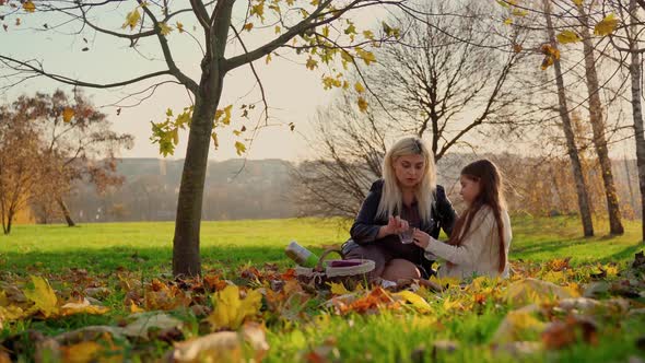 Mother and daughter on picnic at autumn park outdoors. Two females persons spending time together