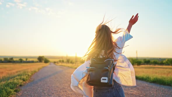 Silhouette From Back of Teenage Girl Who is Waving Her Arms and Running Along an Road in Field