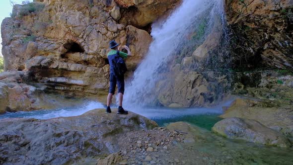 Man is Holding a Mobile Phone and Taking a Photo of a Beautiful Waterfall