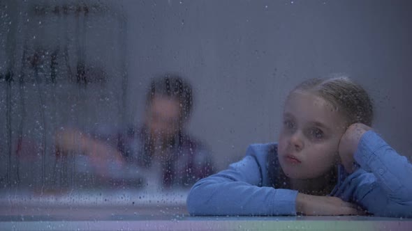 Sad Girl Sitting Behind Rainy Window Alcohol Addicted Father Drinking in Room