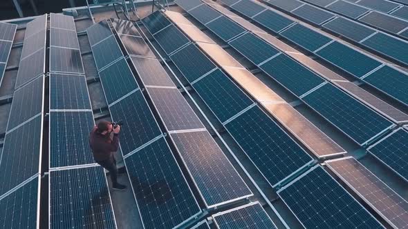 Solar energy farm on roof. Male photographer doing photos among the blue solar panels at sunset. Cle