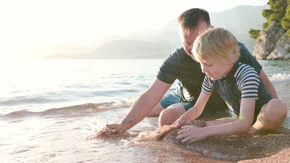 Happy boy and his mature father building a sand and stone castle together