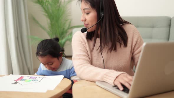 Happy Asian Mother Working on Computer at Home with Her Child Busy Family Mom Giving Call Center