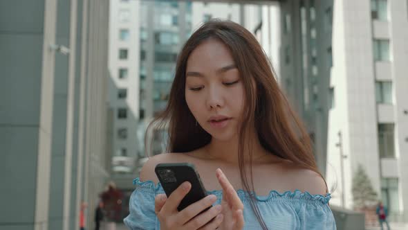 Happy Relaxed Young Asian Woman Holding Smart Phone Looking at Cellphone Screen Laughing Enjoying