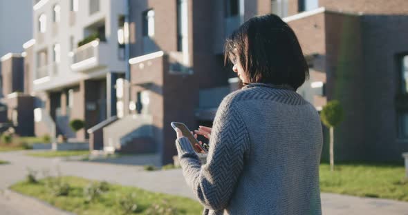 Woman Doing Online Shopping on Smartphone while Walking Through Residential City Street Full