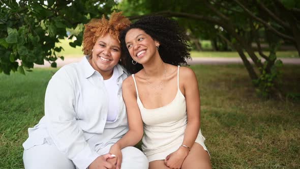 Lovely Beautiful Happy Lesbian African American Couple Sitting on Green Grass Hugging Outside at