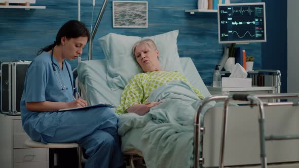 Medical Assistant Talking to Senior Patient with Disease in Bed