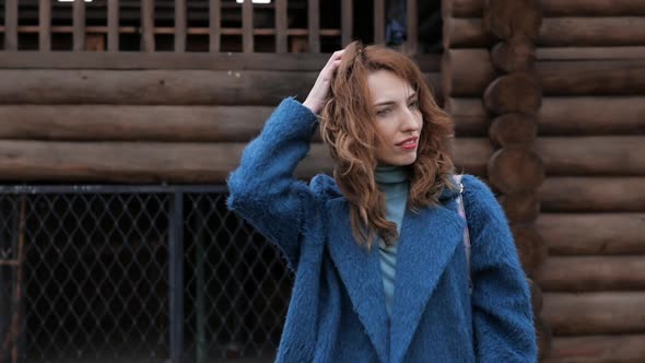 Young Redhaired Woman in a Blue Coat and Walks Against the Backdrop of the Old City