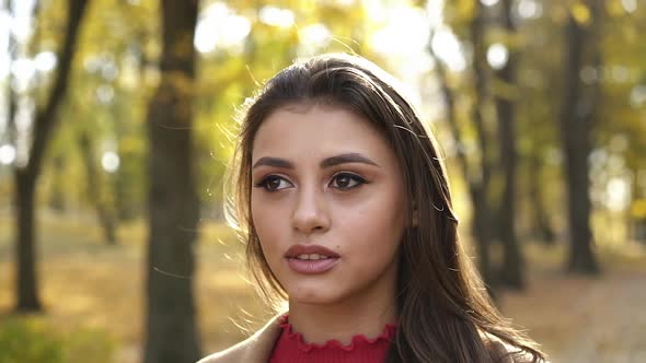 Portrait of Positive Brunette with Makeup Looks at Camera in Sunny Autumn Park